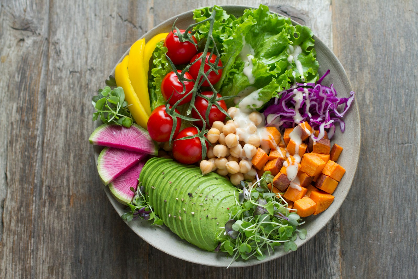 A colorful salad bowl with avocado, chickpeas, radishes, sweet potato, tomatoes, and greens.