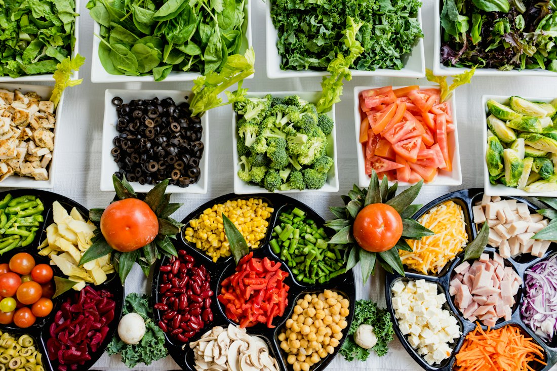 Bowls of fresh greens, vegetables, and colorful ingredients arranged on a white table.